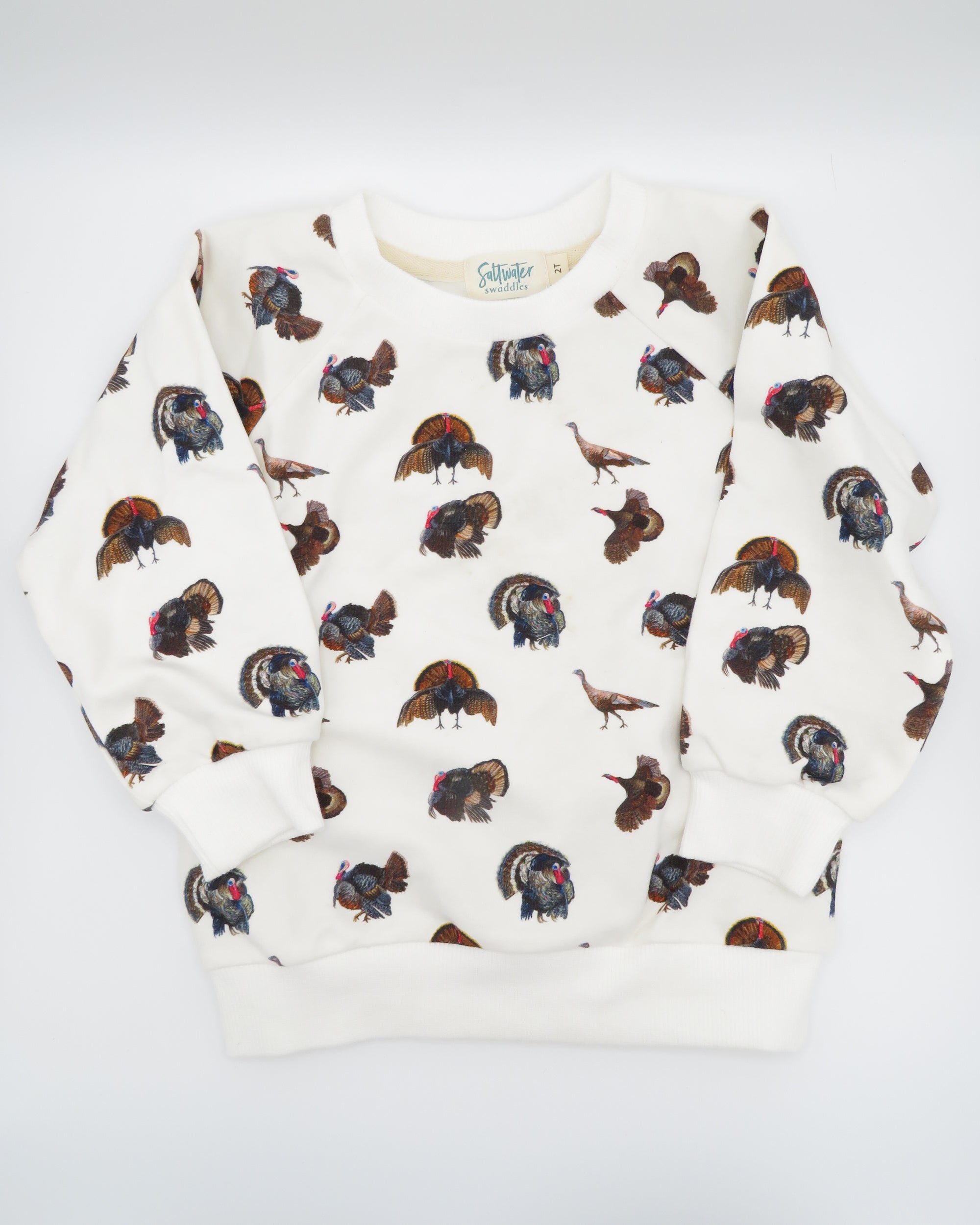 Turkey Trot kids’ drop sleeve sweatshirt in soft white fabric with a playful turkey print, cozy and comfortable for indoors or outdoors. Displayed flat on white background.