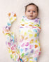 Baby wrapped in a soft Rainbow Row swaddle blanket made from organic white cotton and bamboo, adorned with rainbow-colored heart designs.