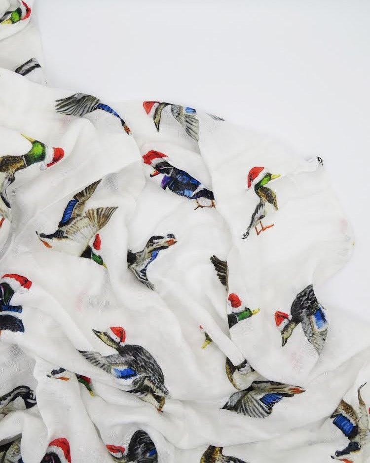 A swaddled baby with a white hat on, wrapped in a blanket with a printed design featuring christmas ducks.