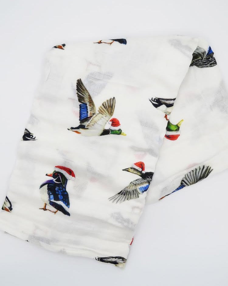 A swaddled baby with a white hat on, wrapped in a blanket with a printed design featuring christmas ducks.