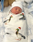 A swaddled baby with a white hat on, wrapped in a blanket with a printed design featuring christmas ducks.