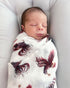 Newborn baby swaddled in a blanket with a gamecock pattern on a gray background.