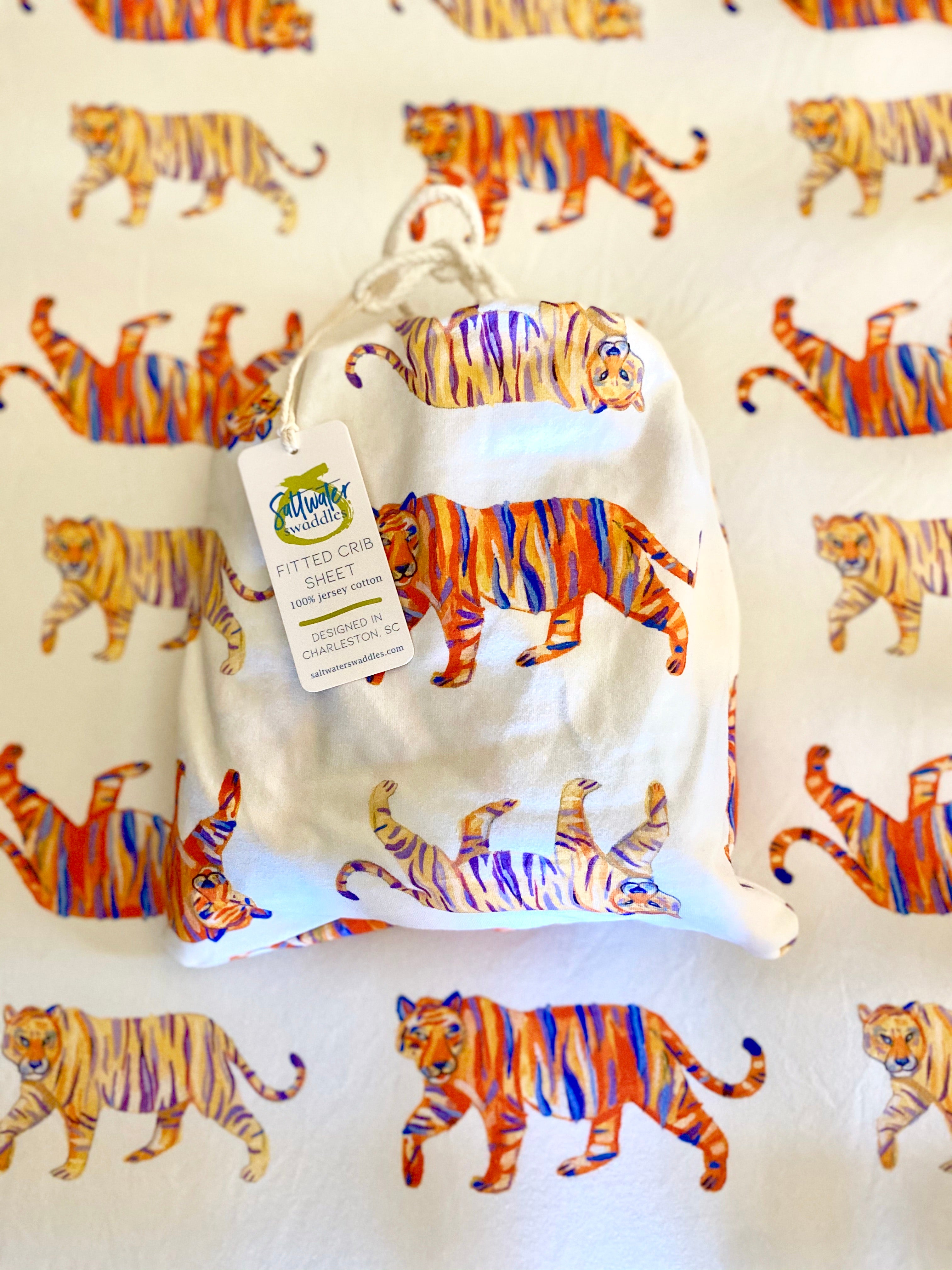 Easy Tiger crib sheet with playful tiger print on soft white jersey cotton fabric, with a baby lying on it. Breathable and gentle, perfect for nurseries, crib sleep, and cozy nap time.